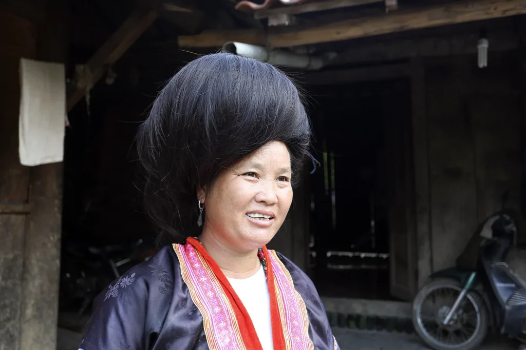 Un chignon, une rencontre Femme hmong rouge portant un volumineux chignon, devant une maison dans un village du col de Ma Thì Hồ.