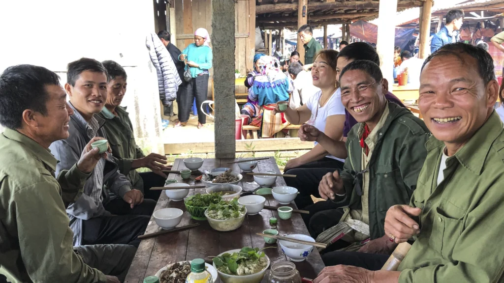 Plusieurs hommes réunis autour de bols et de plats sur une table dans un marché.