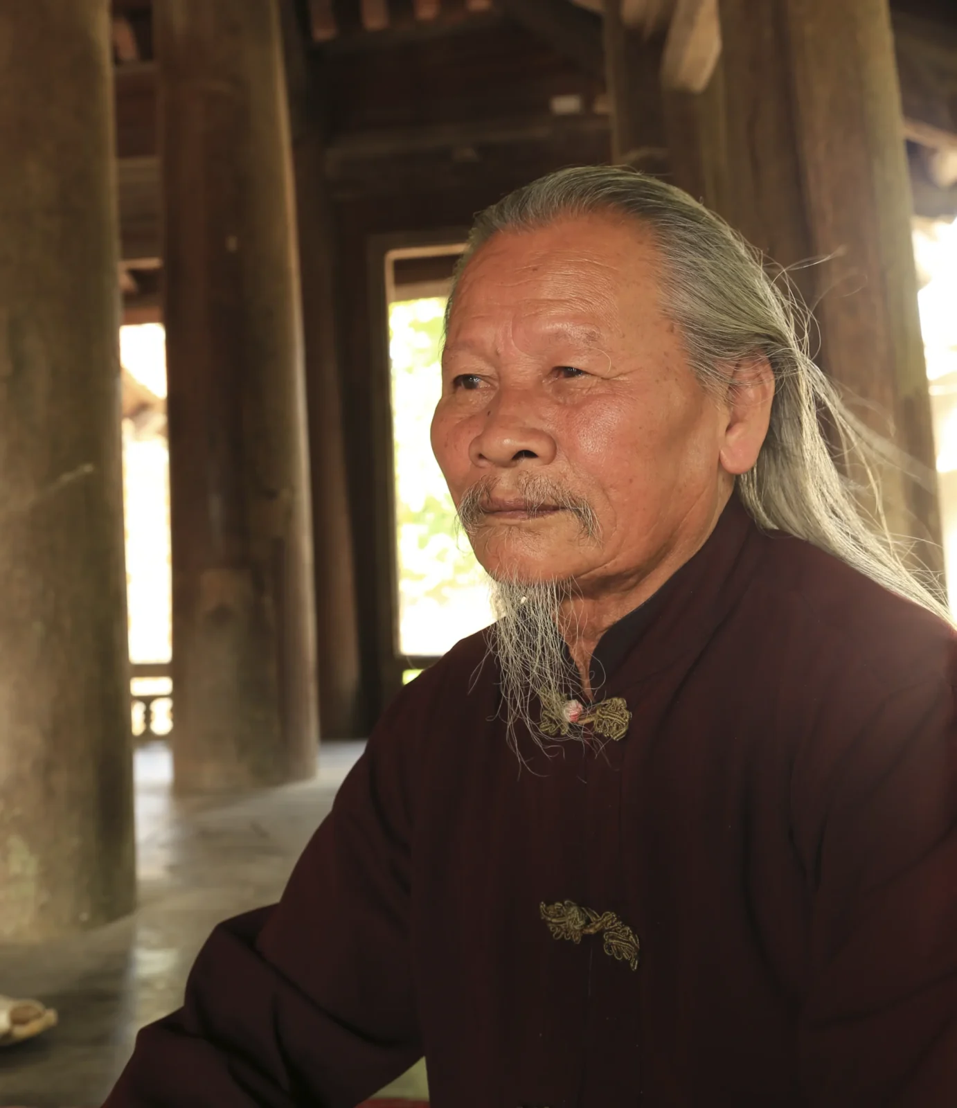 Derrière la porte Portrait de M. Đĩnh, gardien de la maison communale de Mông Phụ à Đường Lâm, parmi les piliers en bois.
