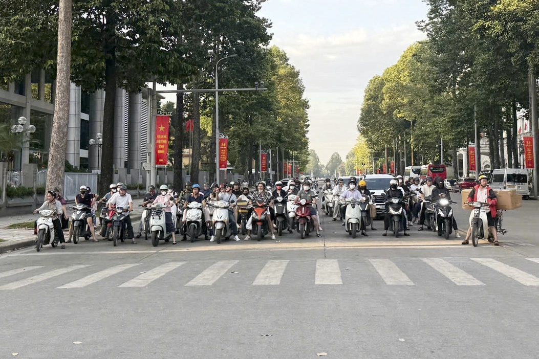 Pourquoi klaxonne-t-on autant au Vietnam ? Des conducteurs à moto attendent devant un passage piéton à un carrefour bordé d’arbres à Hanoi.
