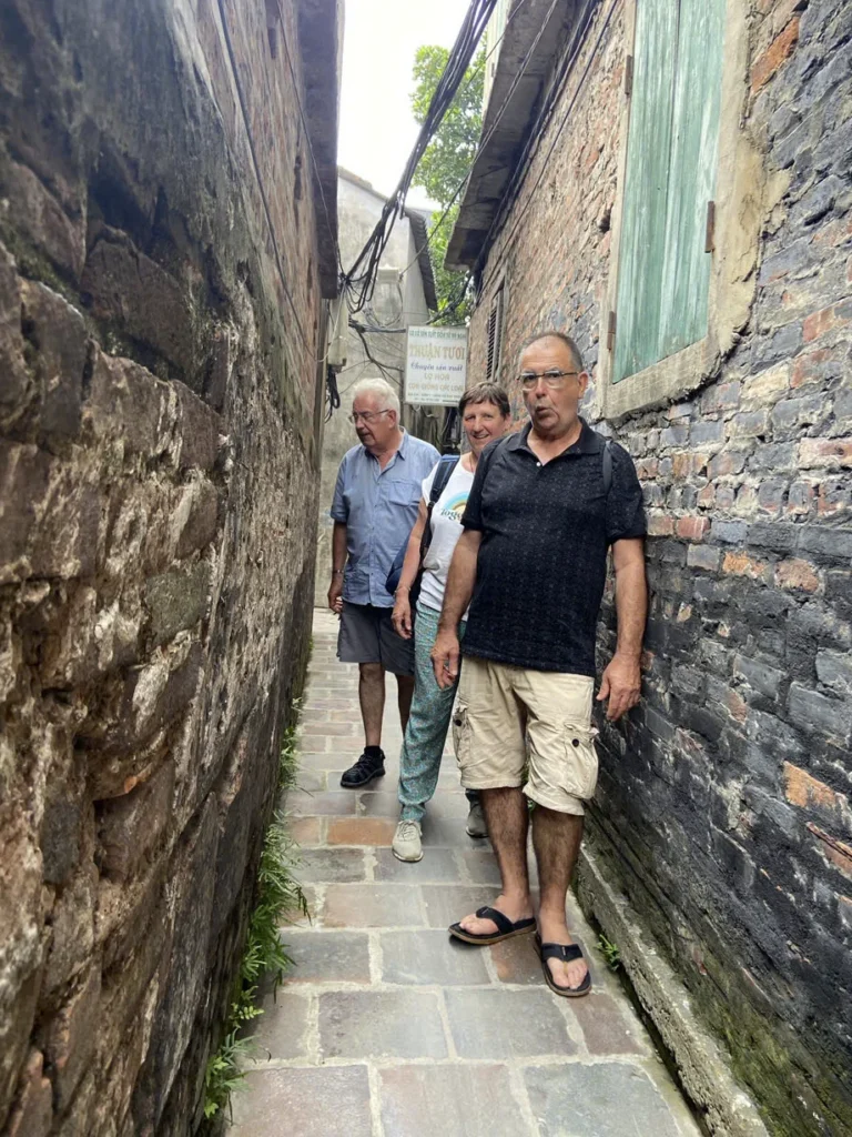 Des visiteurs marchent dans une ruelle étroite de Bát Tràng, entre deux murs de brique.