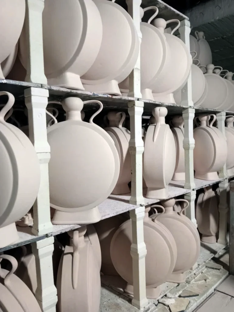 Des vases ronds et plats, munis d’anses, sont disposés sur plusieurs étagères à l’intérieur d’un four de potier à Bát Tràng.