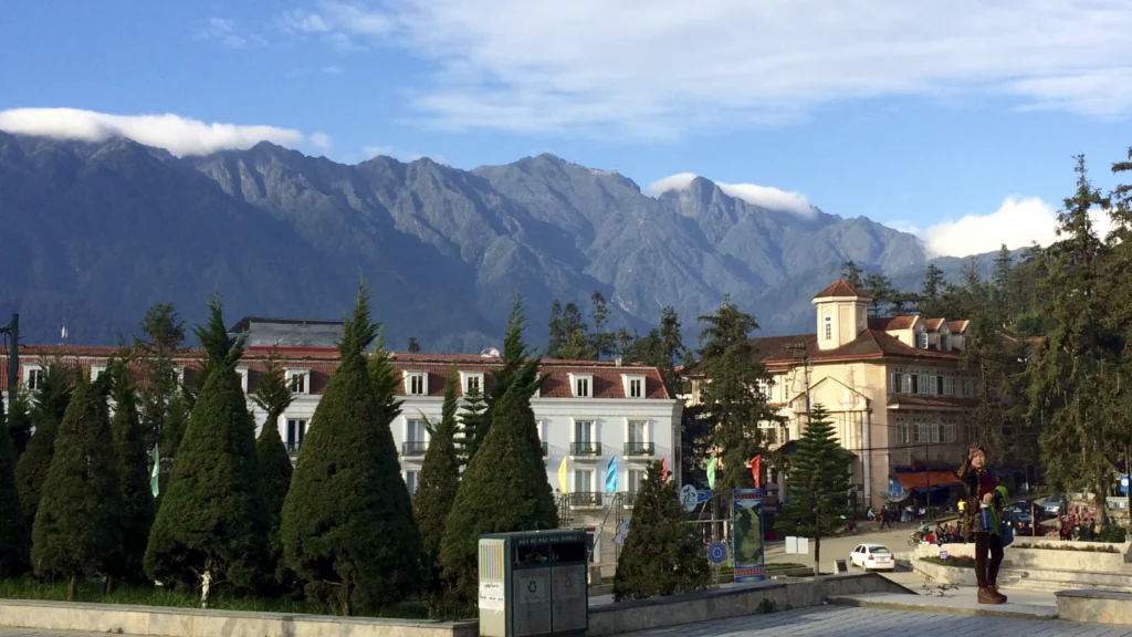 Des bâtiments et une place de Sa Pa devant une longue crête montagneuse sous un ciel bleu.