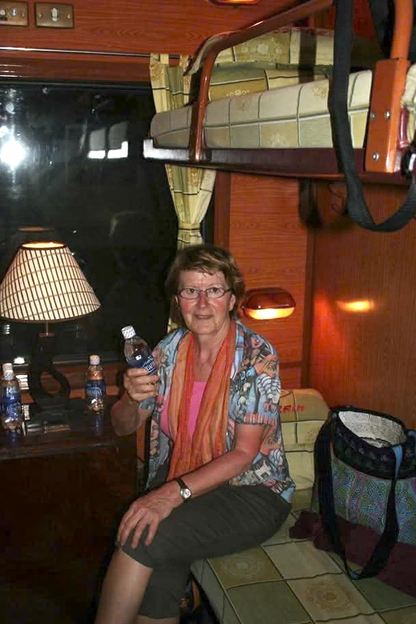 Évelyne assise sur une couchette inférieure, près d’une petite table, dans un compartiment de train.