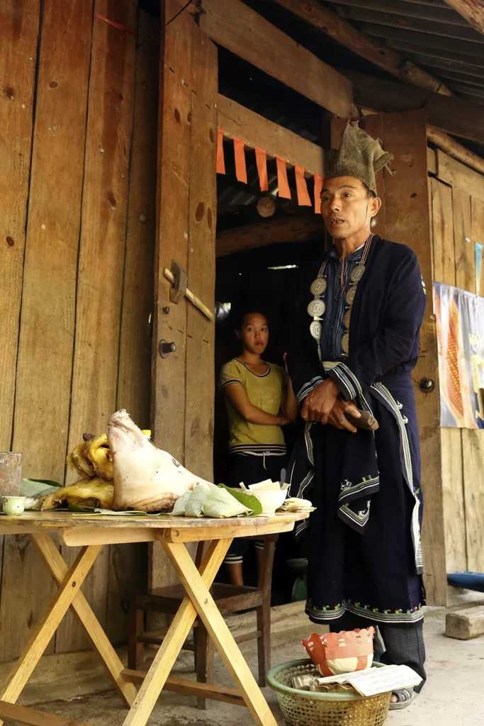 Au détour d’un virage Un maître rituel Dao Tiền en tenue traditionnelle devant la maison d'une famille, en 2014.