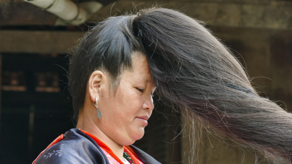 Femme hmong rouge à Ma Thì Hồ, vue de profil, les cheveux déployés et prolongés par du crin de queue de cheval tressé dans sa chevelure.